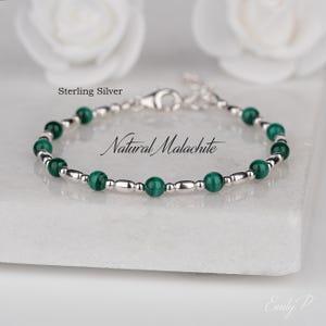 Könnte beinhalten: Ein Armband mit abwechselnd runden grünen Malachitperlen und kleinen silberfarbenen Metallperlen. Das Schmuckstück verfügt über einen Karabinerverschluss und eine kurze Verlängerungskette. Der Text lautet Sterling Silver und Natural Malachite.