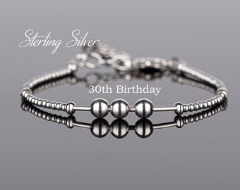 May include: Sterling silver bracelet with three beads and a delicate chain. The bracelet has the text "30th Birthday" on it.