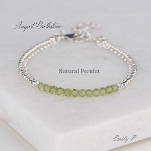 May include: A silver bracelet with a row of green peridot gemstones. The bracelet is labelled "August Birthstone" and "Natural Peridot". The text "Emily P" is also visible in the image.
