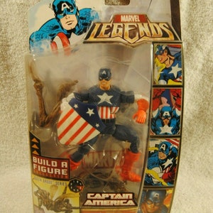 May include: Marvel Legends Captain America action figure in original packaging. The figure is in a dynamic pose, holding a shield with red and white stripes and a blue star field. The packaging includes comic book art and the text "Captain America."
