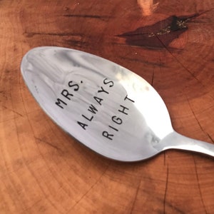 May include: A silver spoon with the words "MRS. ALWAYS RIGHT" engraved on it. The spoon is resting on a wooden surface.