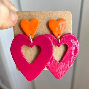May include: A pair of pink heart-shaped earrings with a smaller orange heart on top of each.
