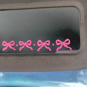 May include: A black car sun visor with four pink bows along the bottom edge.