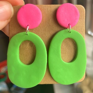 May include: A pair of dangle earrings with a bright green oval shape with a hole in the center and a bright pink circle on top.
