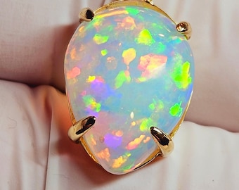 May include: A pear-shaped opal pendant with a gold setting. The opal displays a vibrant play of color, with flashes of green, blue, and pink. The gold setting has a simple, elegant design, with four prongs securing the gemstone.