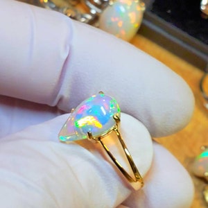 May include: A gold ring with a pear-shaped opal gemstone. The opal is iridescent with flashes of green, blue, and red.