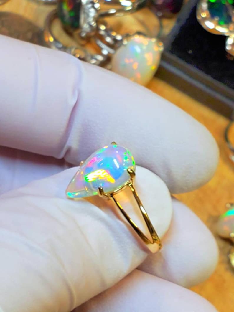 May include: A gold ring with a pear-shaped opal gemstone. The opal is iridescent with flashes of green, blue, and red.