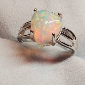 Pode incluir: Um anel de prata com uma gema de opala em forma de p&ecirc;ra. A opala &eacute; iridescente com flashes de verde, azul e vermelho.