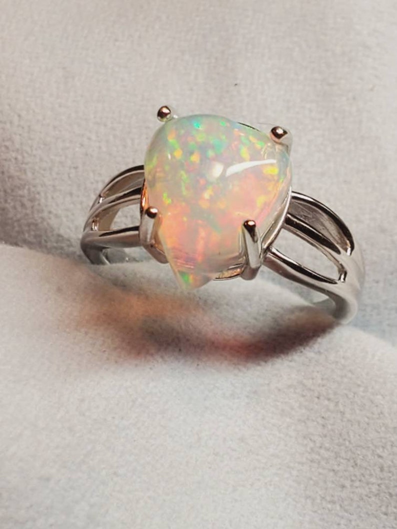 Pode incluir: Um anel de prata com uma gema de opala em forma de p&ecirc;ra. A opala &eacute; iridescente com flashes de verde, azul e vermelho.
