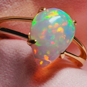 Op de afbeelding: Een gouden ring met een peervormige opaal edelsteen. De opaal heeft een witte basis met flitsen van groen, geel, oranje en rood.