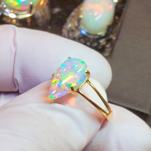 May include: A pear-shaped opal ring set in a gold band. The opal is iridescent with flashes of green, blue, and red.