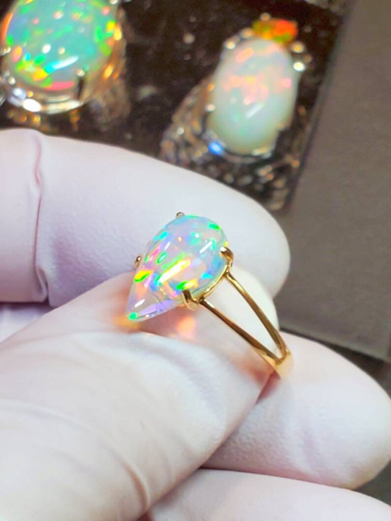 May include: A pear-shaped opal ring set in a gold band. The opal is iridescent with flashes of green, blue, and red.