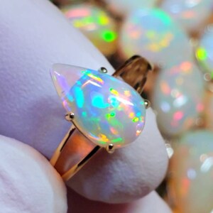 May include: A gold ring with a pear-shaped opal gemstone. The opal is iridescent with flashes of green, blue, and yellow.
