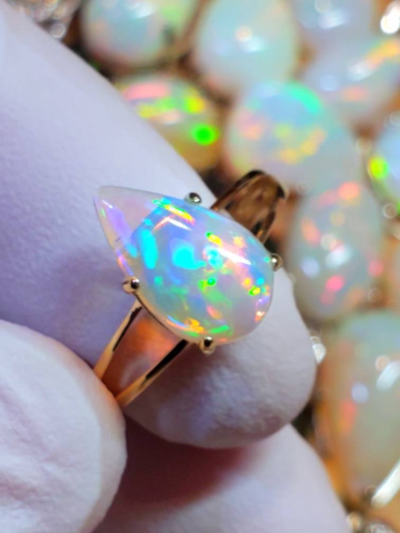 May include: A gold ring with a pear-shaped opal gemstone. The opal is iridescent with flashes of green, blue, and yellow.