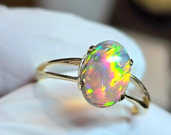 Op de afbeelding: Een gouden ring met een grote ovale opaal. De opaal heeft een regenboog van kleuren, waaronder groen, blauw, rood en geel.