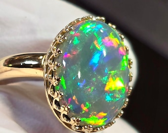 May include: A gold ring with a large oval opal gemstone. The opal has a white base with flashes of green, blue, and red.