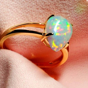 Op de afbeelding: Een gouden ring met een peervormige opaal-edelsteen. De opaal is iriserend met groene, rode en blauwe schittering.