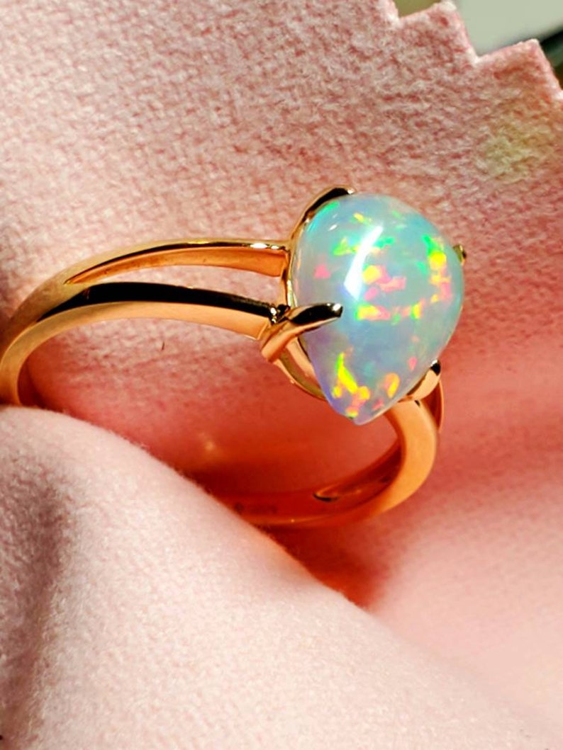 Op de afbeelding: Een gouden ring met een peervormige opaal-edelsteen. De opaal is iriserend met groene, rode en blauwe schittering.