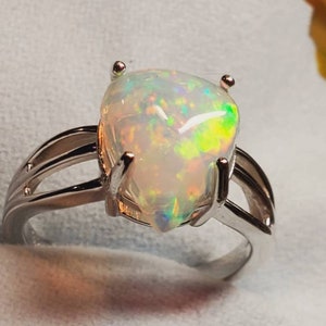 Pode incluir: Um anel de prata com uma gema de opala em forma de p&ecirc;ra. O opala tem uma base branca com flashes de verde, amarelo e azul.