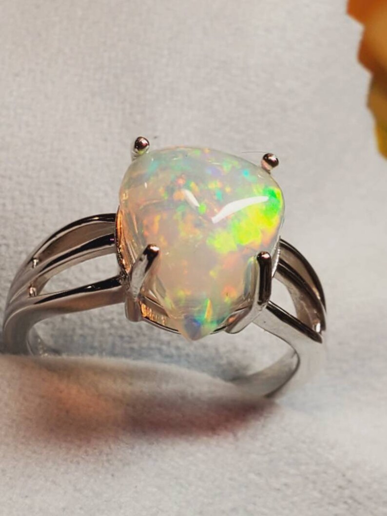 Pode incluir: Um anel de prata com uma gema de opala em forma de p&ecirc;ra. O opala tem uma base branca com flashes de verde, amarelo e azul.
