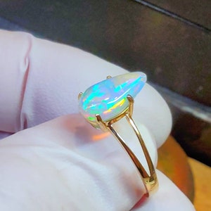 May include: A gold ring with a pear-shaped opal gemstone. The opal is iridescent with flashes of green, blue, and white.