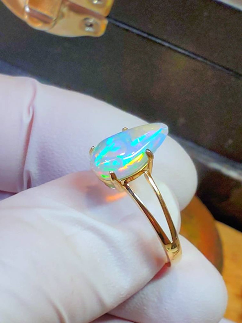 May include: A gold ring with a pear-shaped opal gemstone. The opal is iridescent with flashes of green, blue, and white.