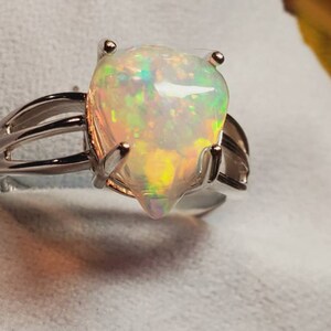 Pode incluir: Um anel de prata com uma gema de opala em forma de p&ecirc;ra. A opala &eacute; iridescente com flashes de verde, azul e amarelo.
