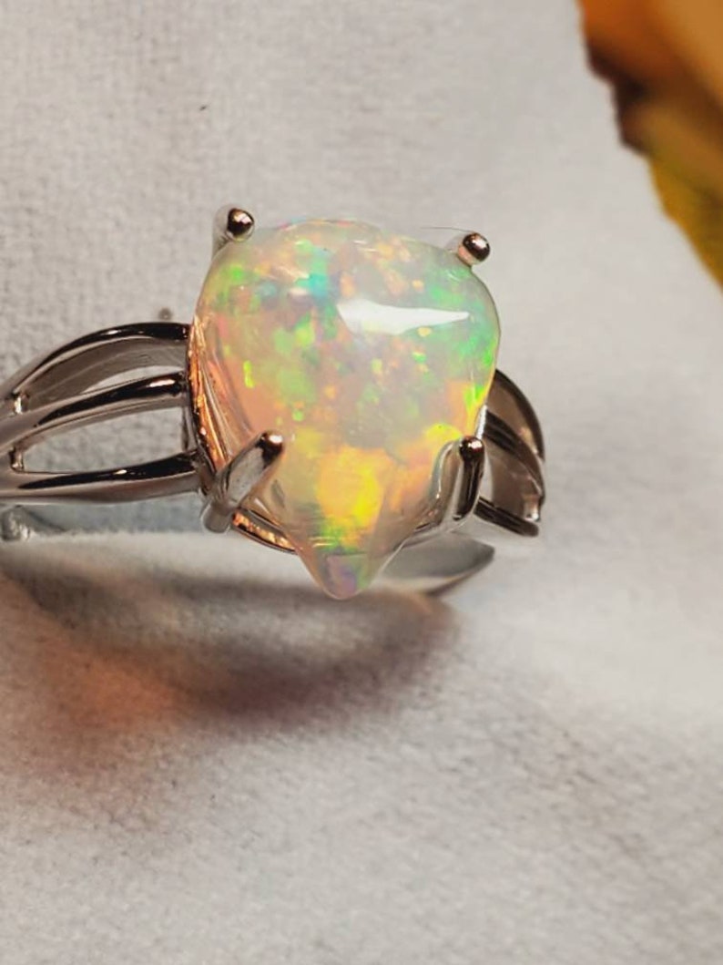 Pode incluir: Um anel de prata com uma gema de opala em forma de p&ecirc;ra. A opala &eacute; iridescente com flashes de verde, azul e amarelo.