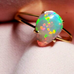 Op de afbeelding: Een gouden ring met een peervormige opaal. De opaal is iriserend met tinten groen, blauw en roze.