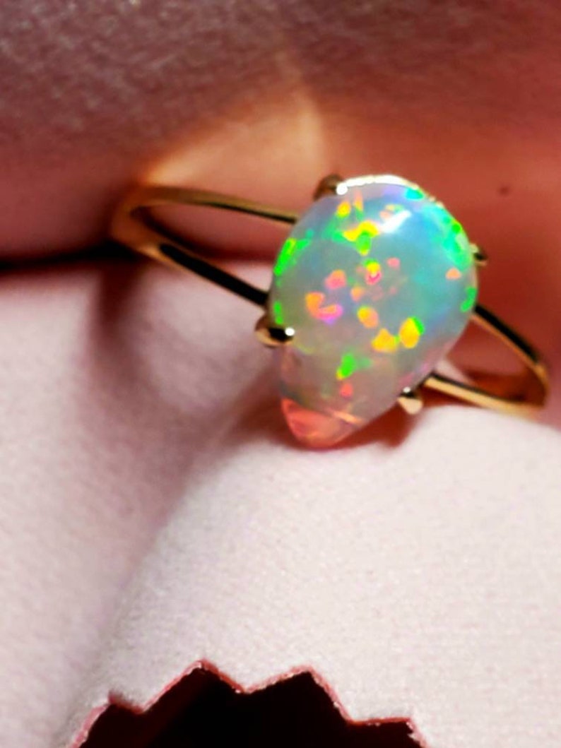 Op de afbeelding: Een gouden ring met een peervormige opaal. De opaal is iriserend met tinten groen, blauw en roze.