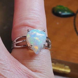 Pode incluir: Um anel de prata com uma gema de opala em forma de l&aacute;grima. A opala &eacute; iridescente com flashes de azul, verde e laranja.