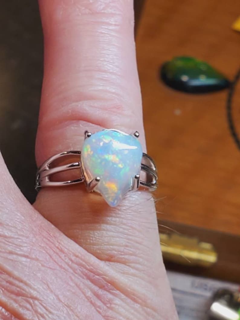 Pode incluir: Um anel de prata com uma gema de opala em forma de l&aacute;grima. A opala &eacute; iridescente com flashes de azul, verde e laranja.