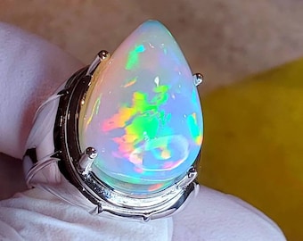 May include: A silver ring with a teardrop-shaped opal gemstone. The opal is iridescent with flashes of green, blue, and pink.