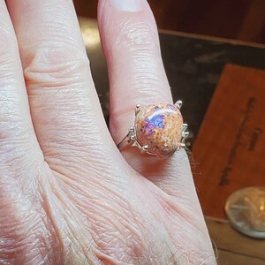 May include: A silver ring with a large, oval-shaped opal gemstone. The opal is a mix of orange, brown, and purple colors.