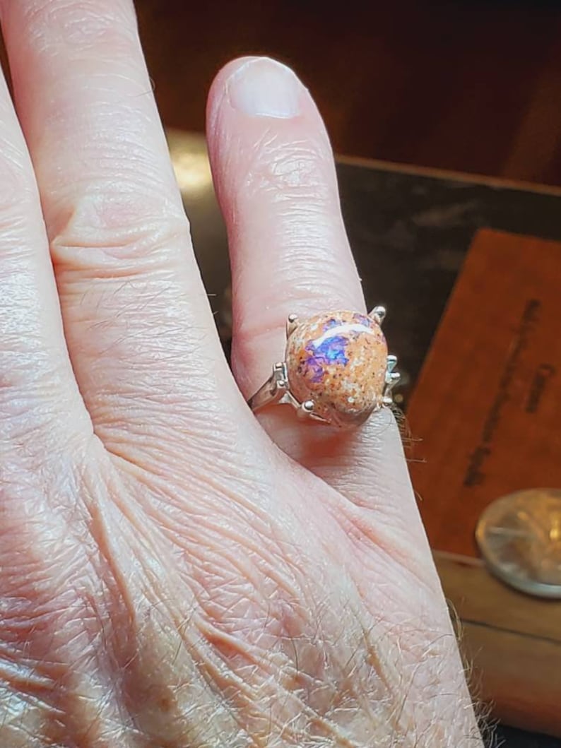 May include: A silver ring with a large, oval-shaped opal gemstone. The opal is a mix of orange, brown, and purple colors.