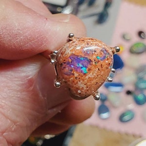 May include: A silver ring with a teardrop-shaped opal stone. The opal is a mix of orange, brown, and purple with iridescent flashes.