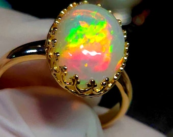 May include: A gold ring with a large oval opal gemstone. The opal has a white base with flashes of green, yellow, and pink.