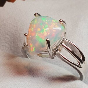 Pode incluir: Um anel de prata com uma gema de opala em forma de p&ecirc;ra. A opala &eacute; branca com flashes de verde, laranja e vermelho.
