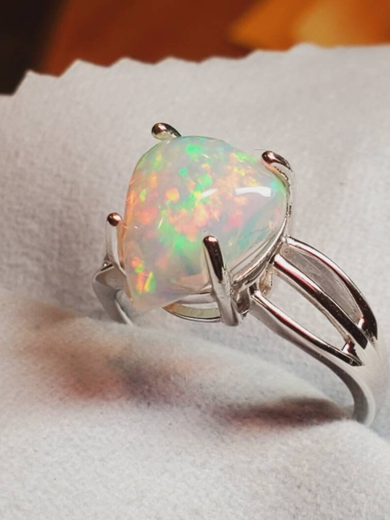Pode incluir: Um anel de prata com uma gema de opala em forma de p&ecirc;ra. A opala &eacute; branca com flashes de verde, laranja e vermelho.