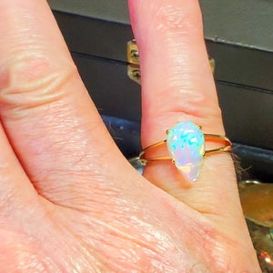 May include: A gold ring with a teardrop-shaped opal gemstone. The opal is iridescent with shades of blue, green, and white.