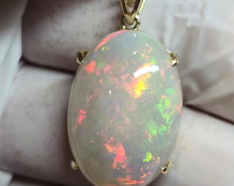 May include: A gold chain necklace with a large oval opal pendant. The opal is white with flashes of green, red, and orange.