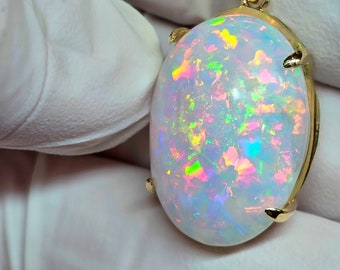 Op de afbeelding: Een witte opaal hanger met een gouden zetting. De opaal heeft een regenboog van kleuren, waaronder roze, groen en blauw.