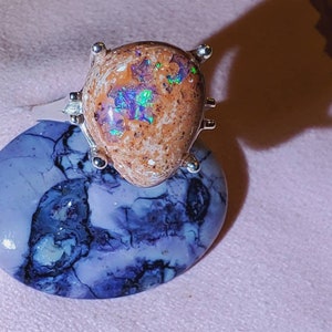 May include: A silver ring with a brown opal gemstone set in a prong setting. The opal has iridescent flashes of green, blue, and purple.