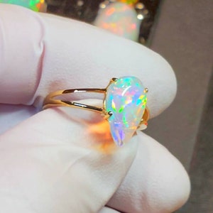 May include: A gold ring with a teardrop-shaped opal gemstone. The opal is iridescent with flashes of green, blue, and red.