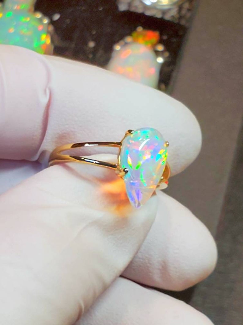 May include: A gold ring with a teardrop-shaped opal gemstone. The opal is iridescent with flashes of green, blue, and red.