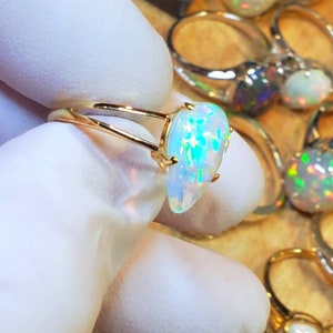 May include: A gold ring with a white opal gemstone. The opal has a teardrop shape and displays a rainbow of colors.