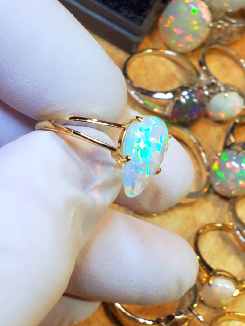 May include: A gold ring with a white opal gemstone. The opal has a teardrop shape and displays a rainbow of colors.