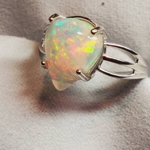 Pode incluir: Um anel de prata com uma gema de opala em forma de p&ecirc;ra. O opala &eacute; iridescente com flashes de verde, azul e vermelho.