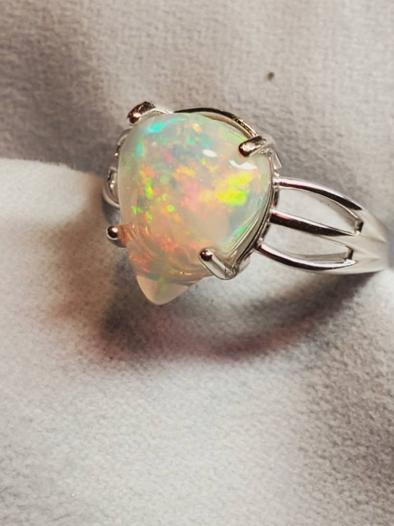 Pode incluir: Um anel de prata com uma gema de opala em forma de p&ecirc;ra. O opala &eacute; iridescente com flashes de verde, azul e vermelho.