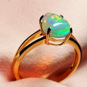 Op de afbeelding: Een gouden ring met een peervormige opaal-edelsteen. De opaal heeft een witte basis met groene, blauwe en roze schittering.